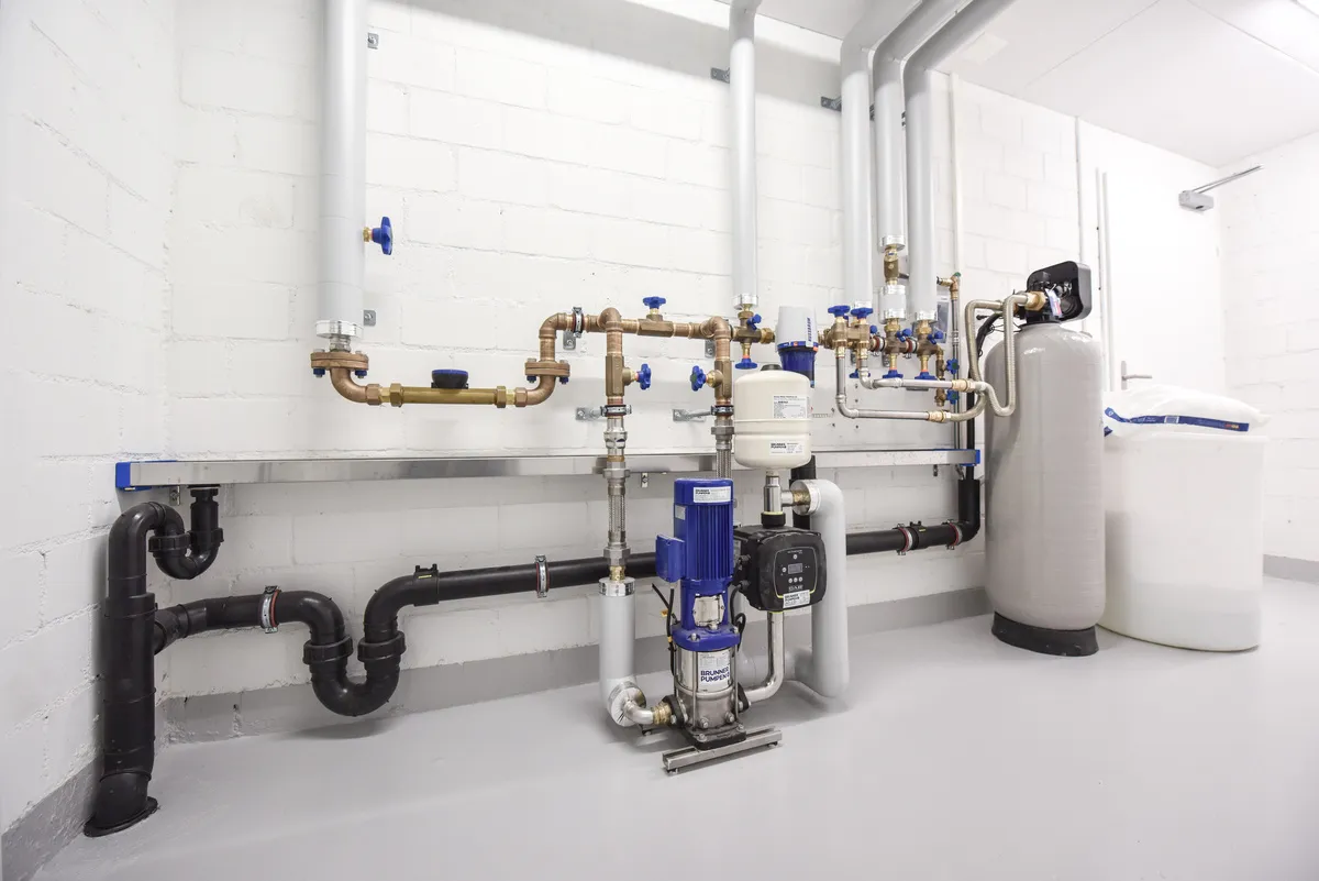 Système de plomberie avec adoucisseur d'eau et tuyauterie en cuivre installé dans une salle technique.